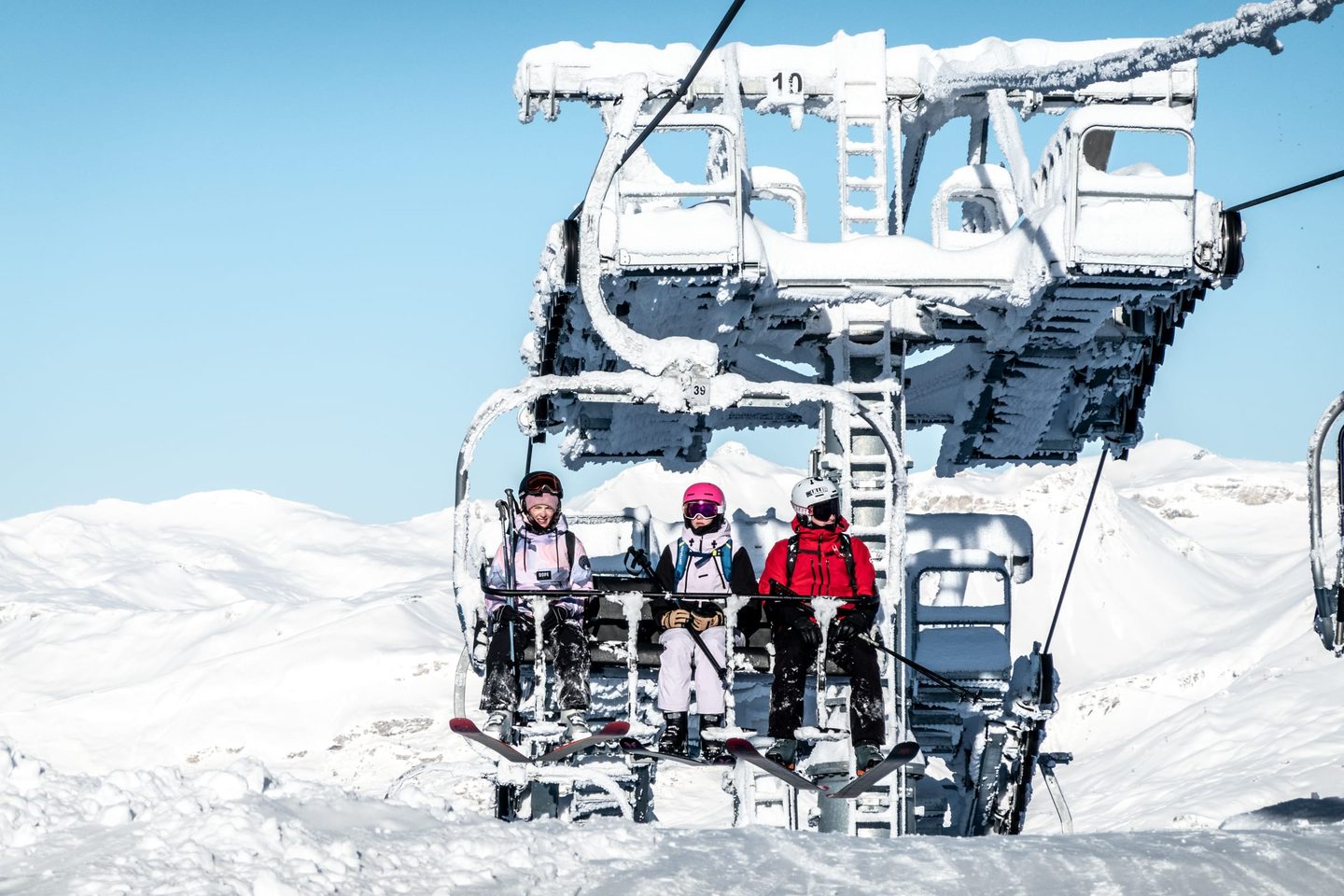 Trois skieurs sur un télésiège entièrement recouvert de givre, face au domaine enneigé